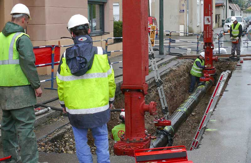 Technicians hot tapping a pipeline excavated under a sidewalk 