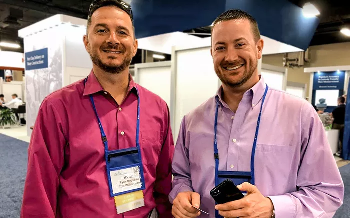 Two TDW employees pictured at an industry trade show with exhibit booths behind them