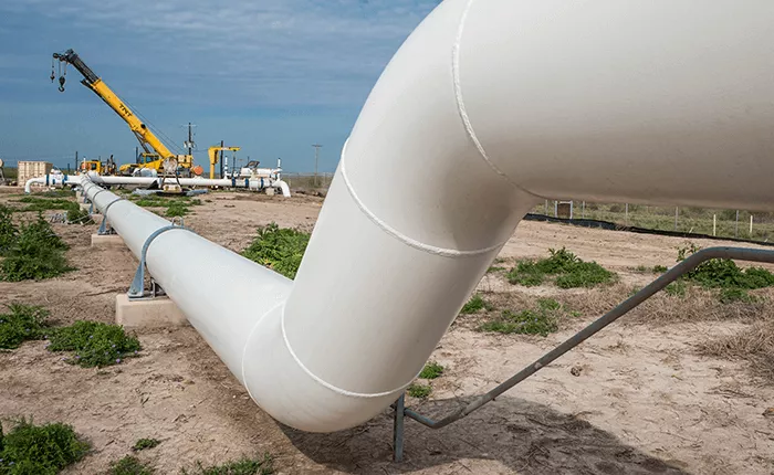 Pipeline shown in a field with a pipeline service job in progress in the background